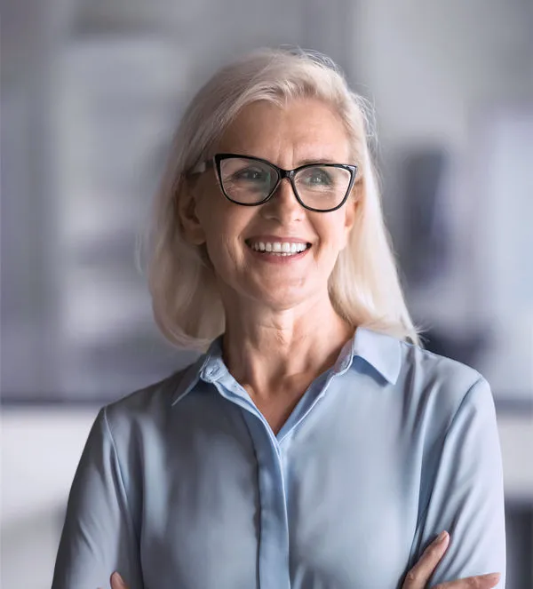 Reife weibliche Führungskraft mit Brille lächelt selbstbewusst in moderner Büroumgebung – Symbolbild für Erfahrung, Leadership und Führungskräfte Coaching.