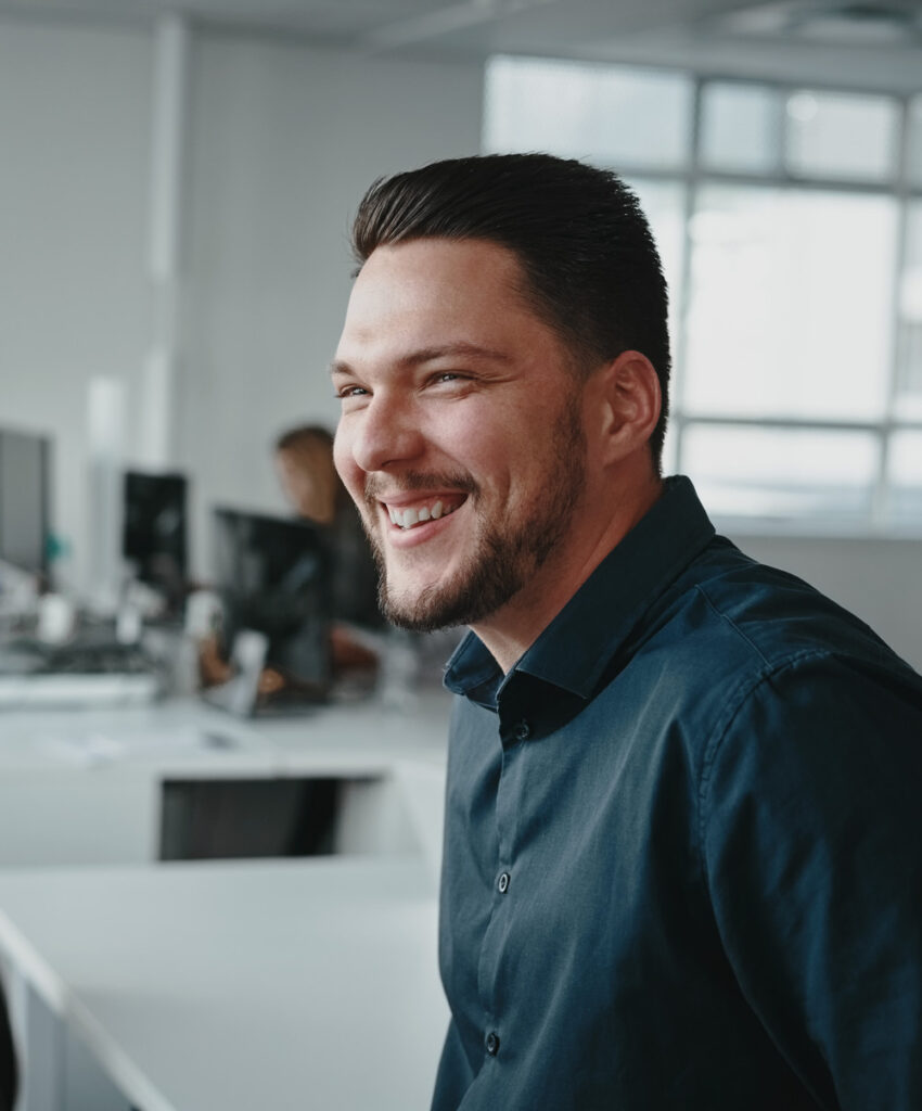 Junge männliche Führungskraft in entspannter Bürosituation mit positiver Ausstrahlung – Sinnbild für moderne Leadership-Kultur und Coaching im Unternehmenskontext.